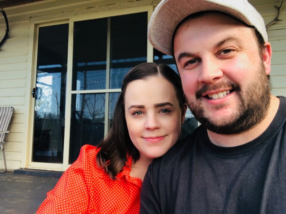 A man and a woman smile at the camera while sitting outside