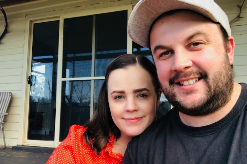 A man and a woman smile at the camera while sitting outside