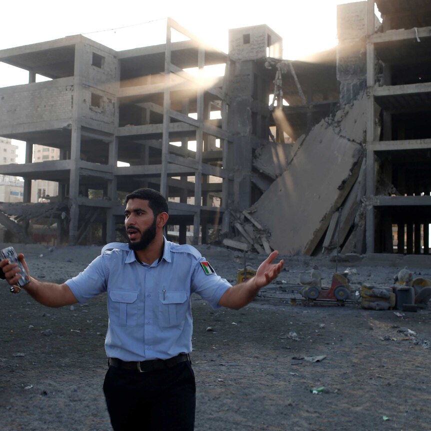 A policeman gestures outside a destroyed building while another man nearby points at the sky.