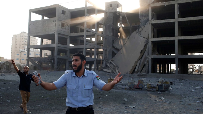 A policeman gestures outside a destroyed building while another man nearby points at the sky.