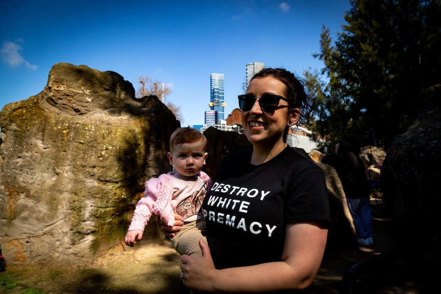 A person with a baby in front of the Melbourne skyline.