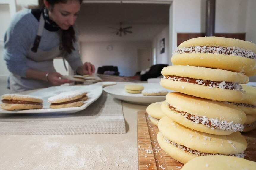 A stack of freshly-made alfajores - a sandwich cookie with caramel sauce - sits on a kitchen table next to Camila Del Valle.