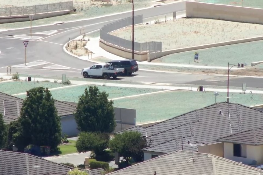 A white ute stopped at a roundabout with a dark vehicle parked next to it.