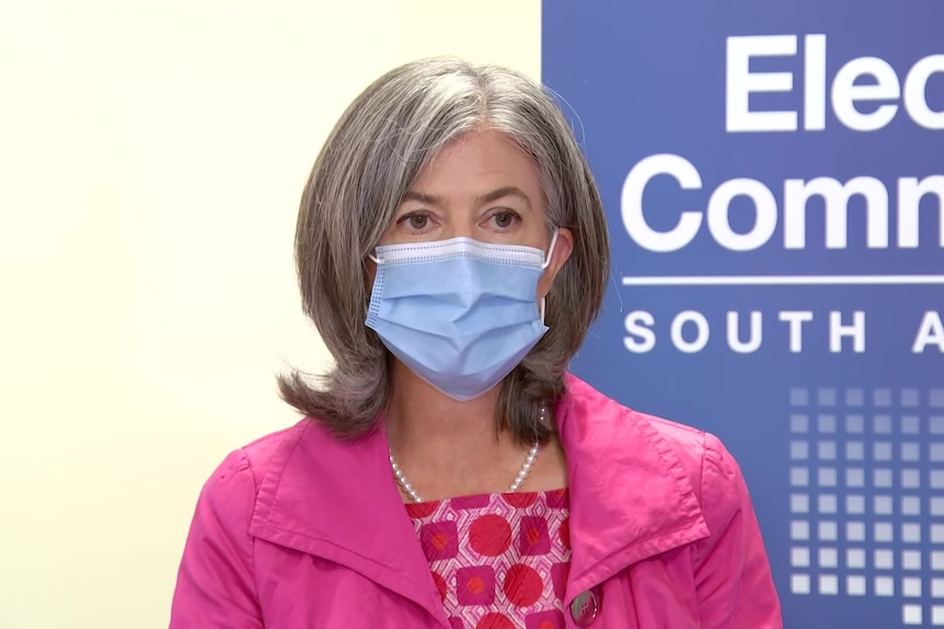 A woman with grey hair wearing a face mask and a pink jacket