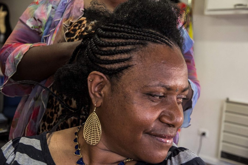 Close up of South Sudanese hairdresser using hair extensions to do corn rows in a customer's hair