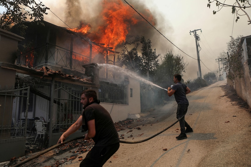 Two men spray a burning house with water from a hose