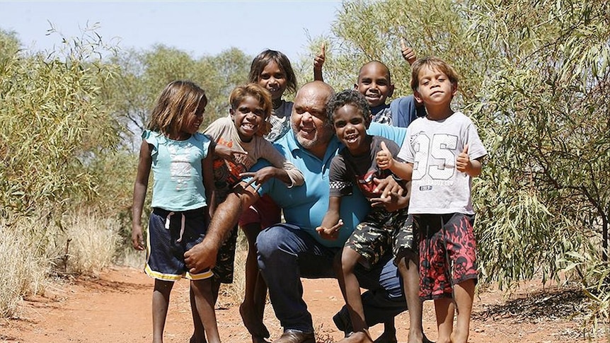 Noel Pearson and six local children stand on a dirt road in the bush
