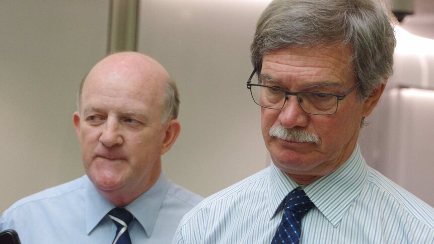 Mike Nahan looks down with John Day in the background at a media conference.