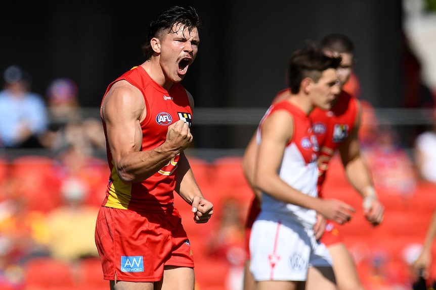 A Gold Coast Suns AFL player pumps his right fist as he celebrates a goal against the Sydney Swans.