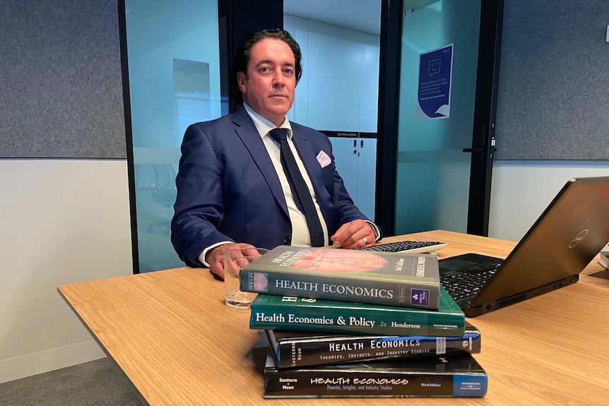 Professor Luke Connelly sits at a desk with a laptop and textbooks in front of him.