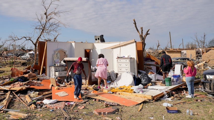 Four people are pictured searching for belongings in the wreckage of a home.