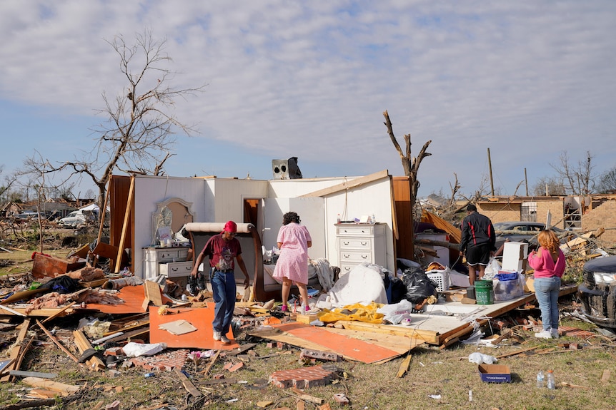 Four people are pictured searching for belongings in the wreckage of a home.