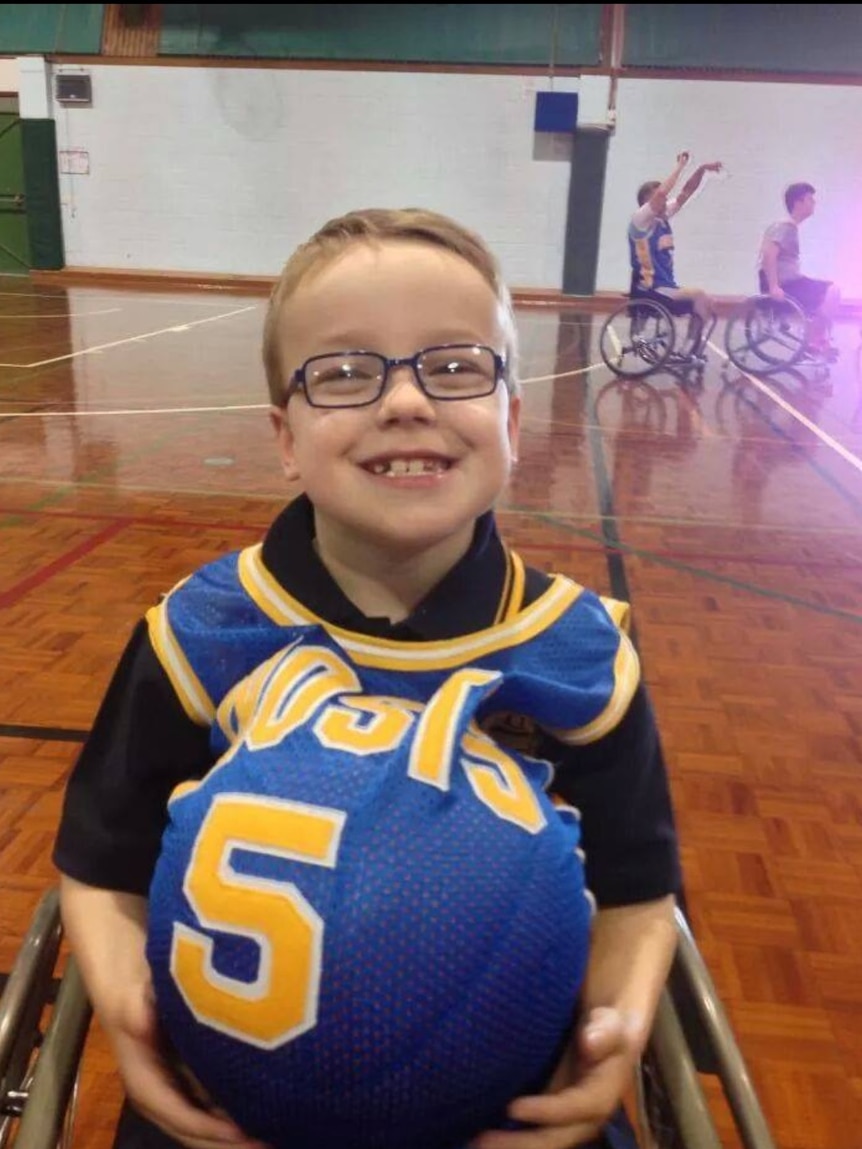 A small boy grins at the camera as he holds a basketball