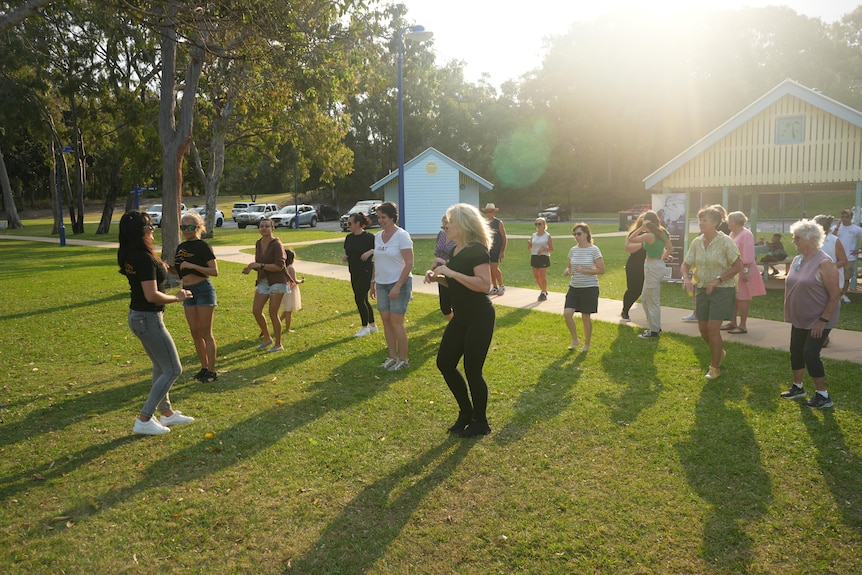 A group of about 20 people dance in a park at sunset