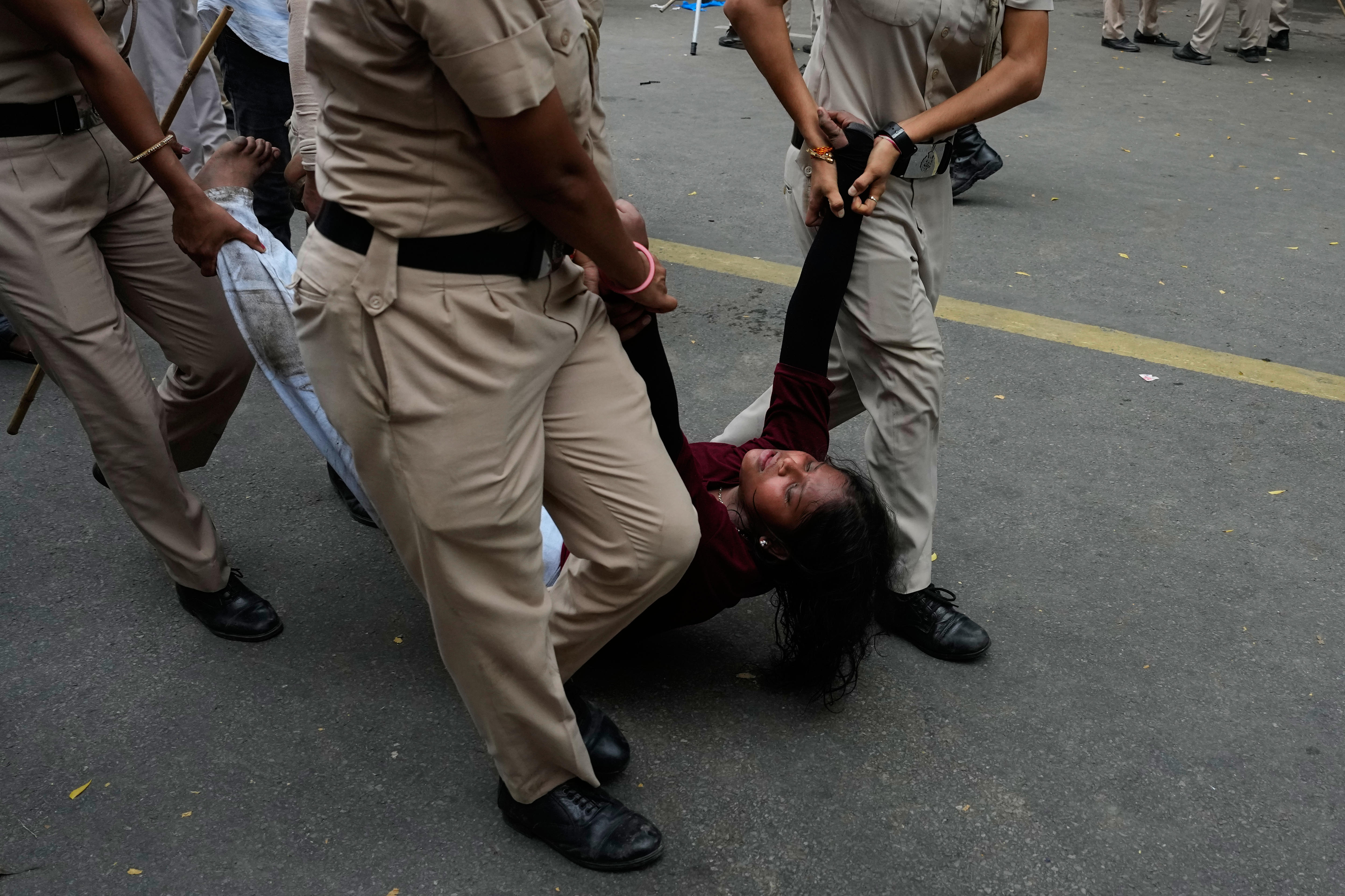 India police carry a woman along a road by her arms and legs. 