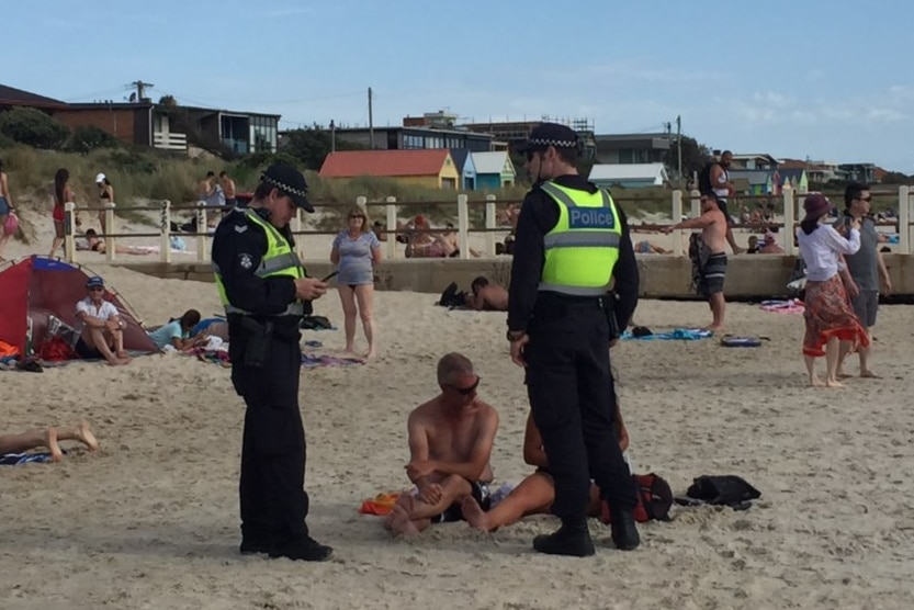 Two police speak to two beachgoers at Chelsea beach.