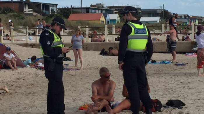 Two police speak to two beachgoers at Chelsea beach.