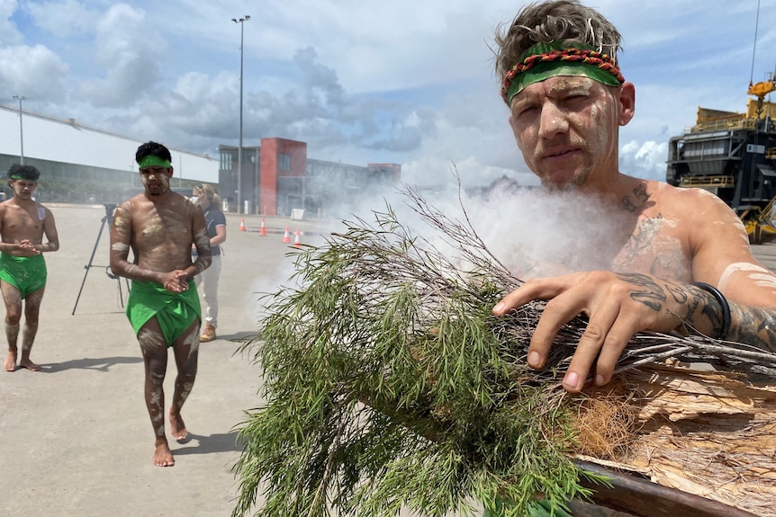 A close of up of a man with traditional Indigenous body paint taking part in a smoking ceremony.