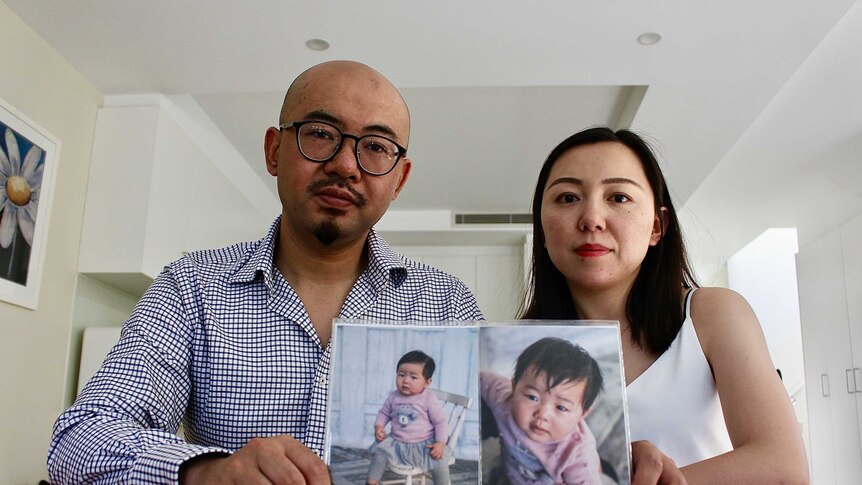Two parents hold up two photos of their baby daughter