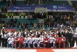 Wide shot of a large group of hockey players and officials kneeling and standing on ice.
