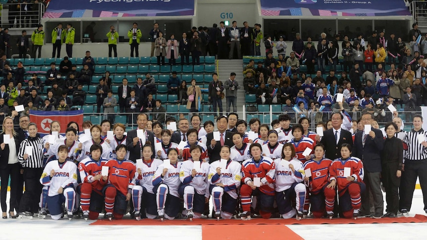 Wide shot of a large group of hockey players and officials kneeling and standing on ice.