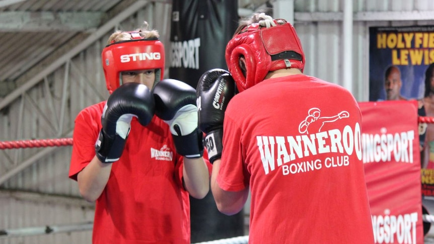 Two teenagers wearing gloves boxing in a gymnasium.