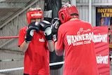 Two teenagers wearing gloves boxing in a gymnasium.
