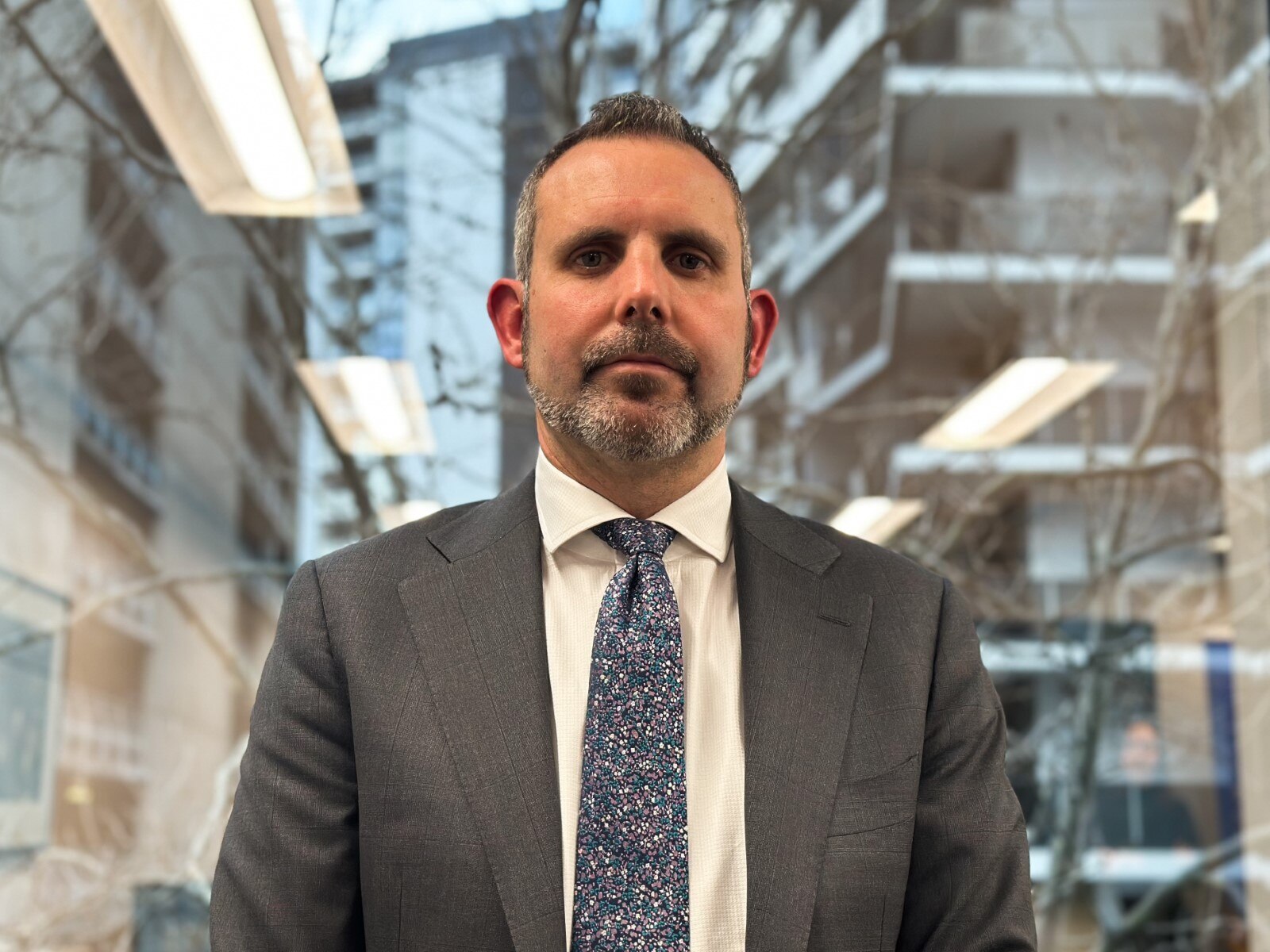 A man in a grey suit with a speckled tie.