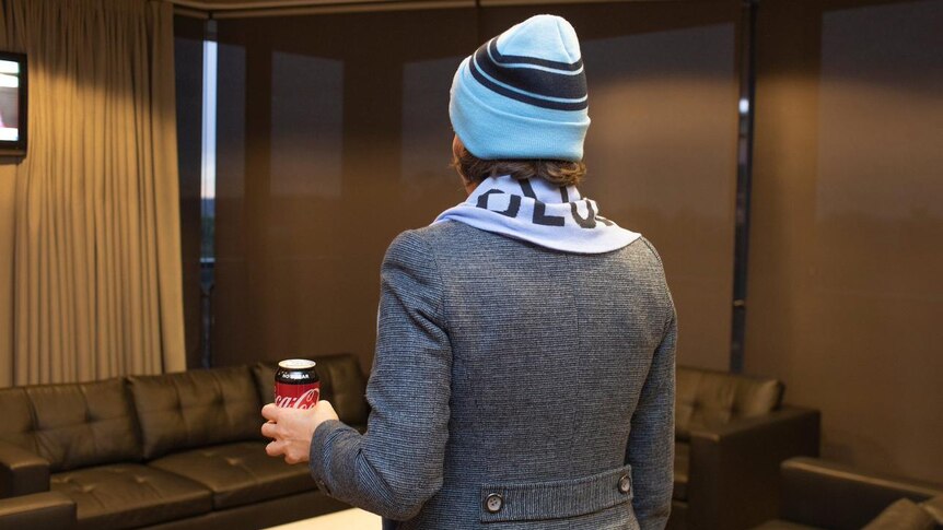 a photo of the back of premier Gladys Berijiklin holding a can of coca cola wearing a beanie and scarf and grey jacket
