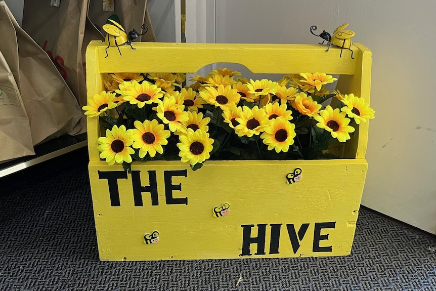 A yellow toolbox with sunflowers inside it and bee models