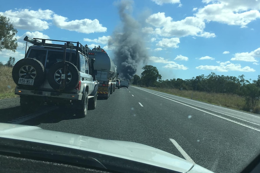 A huge plume of smoke as seen from inside a car on a highway.