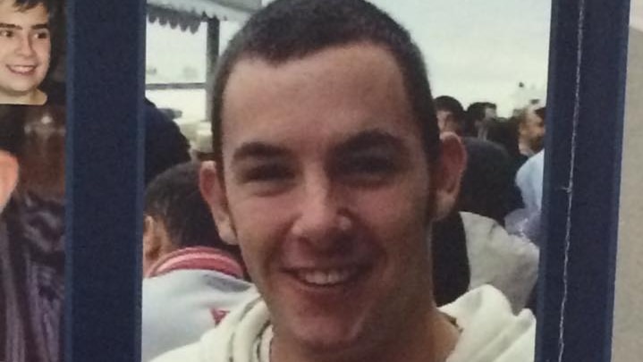 A photo on a missing person poster of a smiling man with short hair wearing a white jumper.