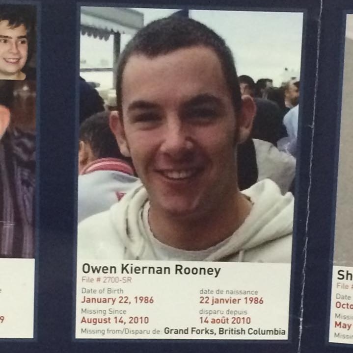 A photo on a missing person poster of a smiling man with short hair wearing a white jumper.