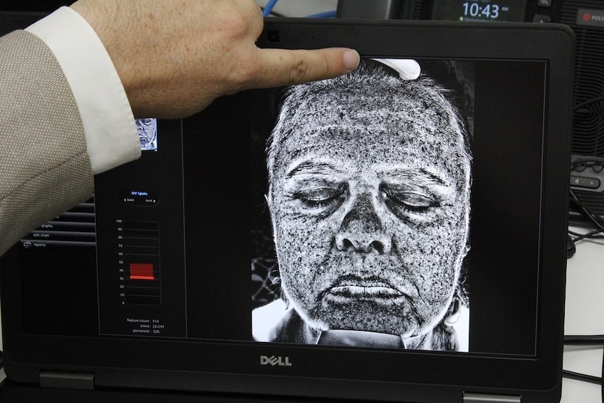 Man sits at a large white contraption that's a uv camera.