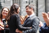 Jacinda Ardern, left, wears a black blazer and has one hand on Clarke Gayford's waist, right. They smile at each other.
