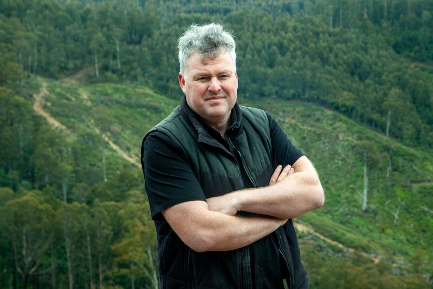 Chris Taylor standing with his arms crossed in front of a section of logged forest.