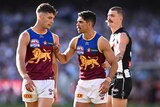 Two Brisbane Lions players stand together at the MCG, with one putting his hand up against his teammate as he speaks to him.