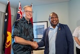 An Australian man wearing a blue pacific themed shirt with a Papua New Guinean man in suit shaking hands
