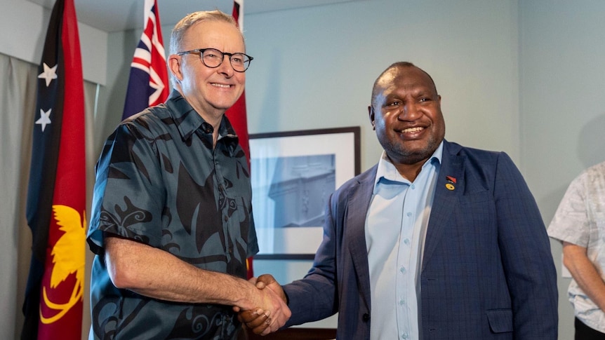 An Australian man wearing a blue pacific themed shirt with a Papua New Guinean man in suit shaking hands