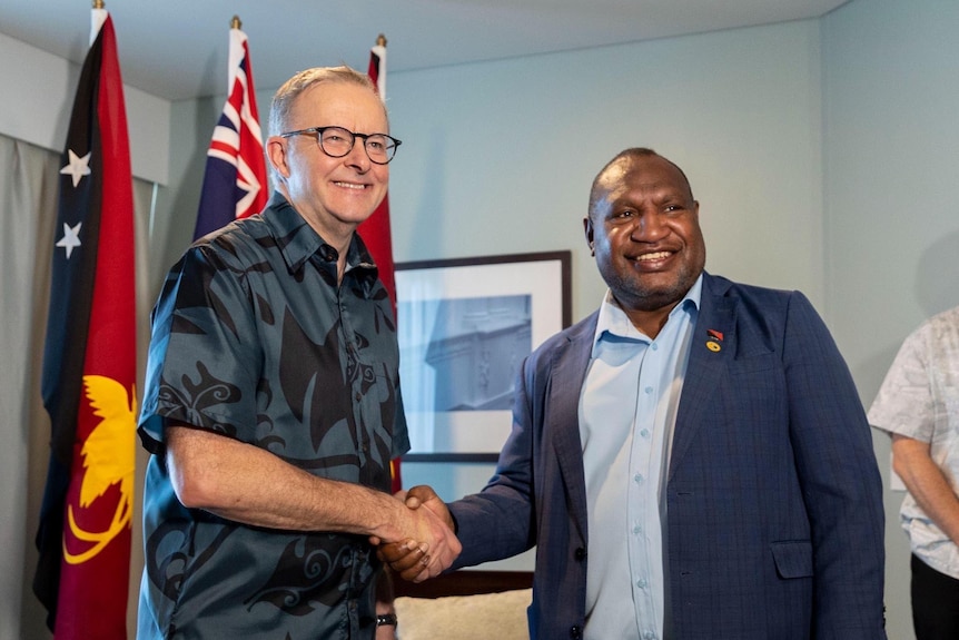 An Australian man wearing a blue pacific themed shirt with a Papua New Guinean man in suit shaking hands