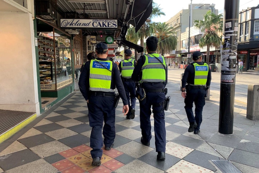 A group of police in high-vis vests on a city street photographed from the rear