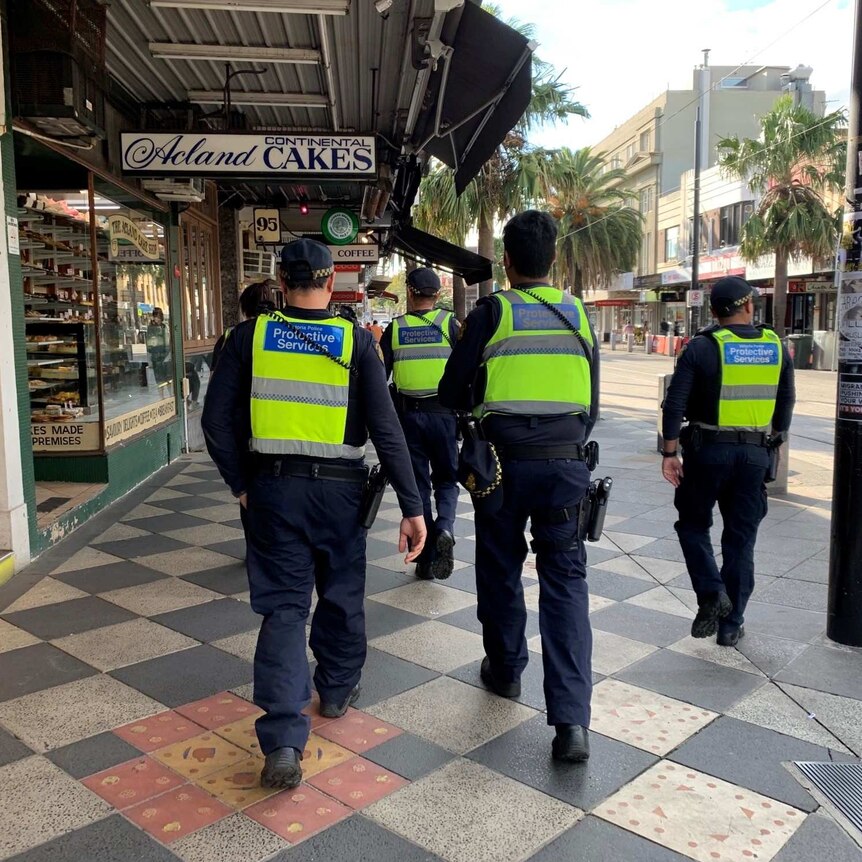 A group of police in high-vis vests on a city street photographed from the rear