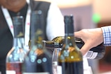 A close up of a wine being poured, other wines with screw tops,  man with a lanyard in blurred foreground.