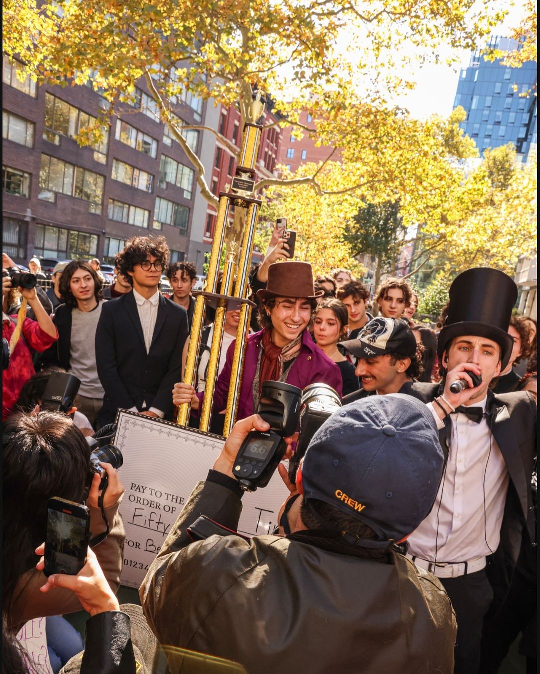 A man dressed up like Chalamet's Willy Wonka holding up a trophy with people surrounding him