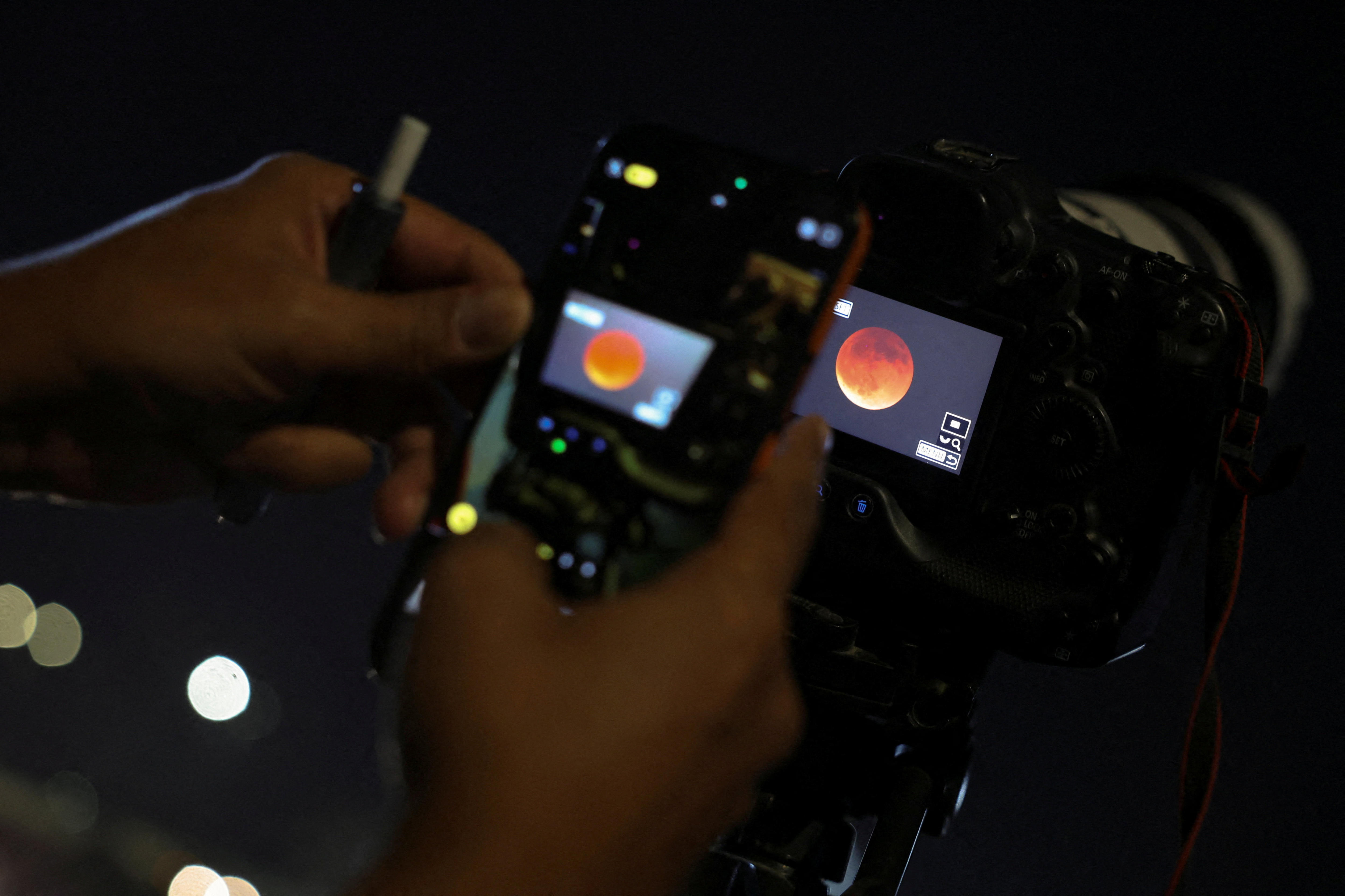 A photo of a blood moon is seen through a person’s digital camera screen