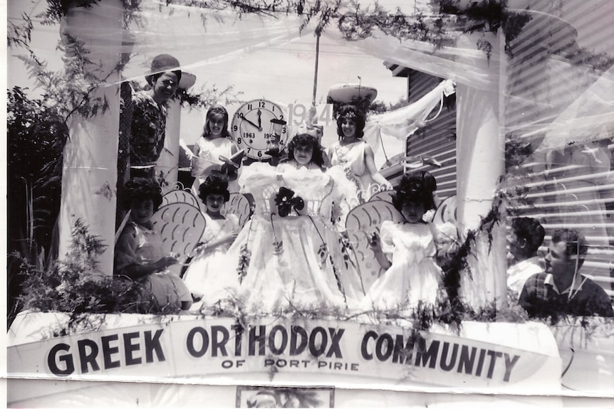 Women and girls wearing angel costumes stand on the back of a truck that is dressed up for a Christmas pageant