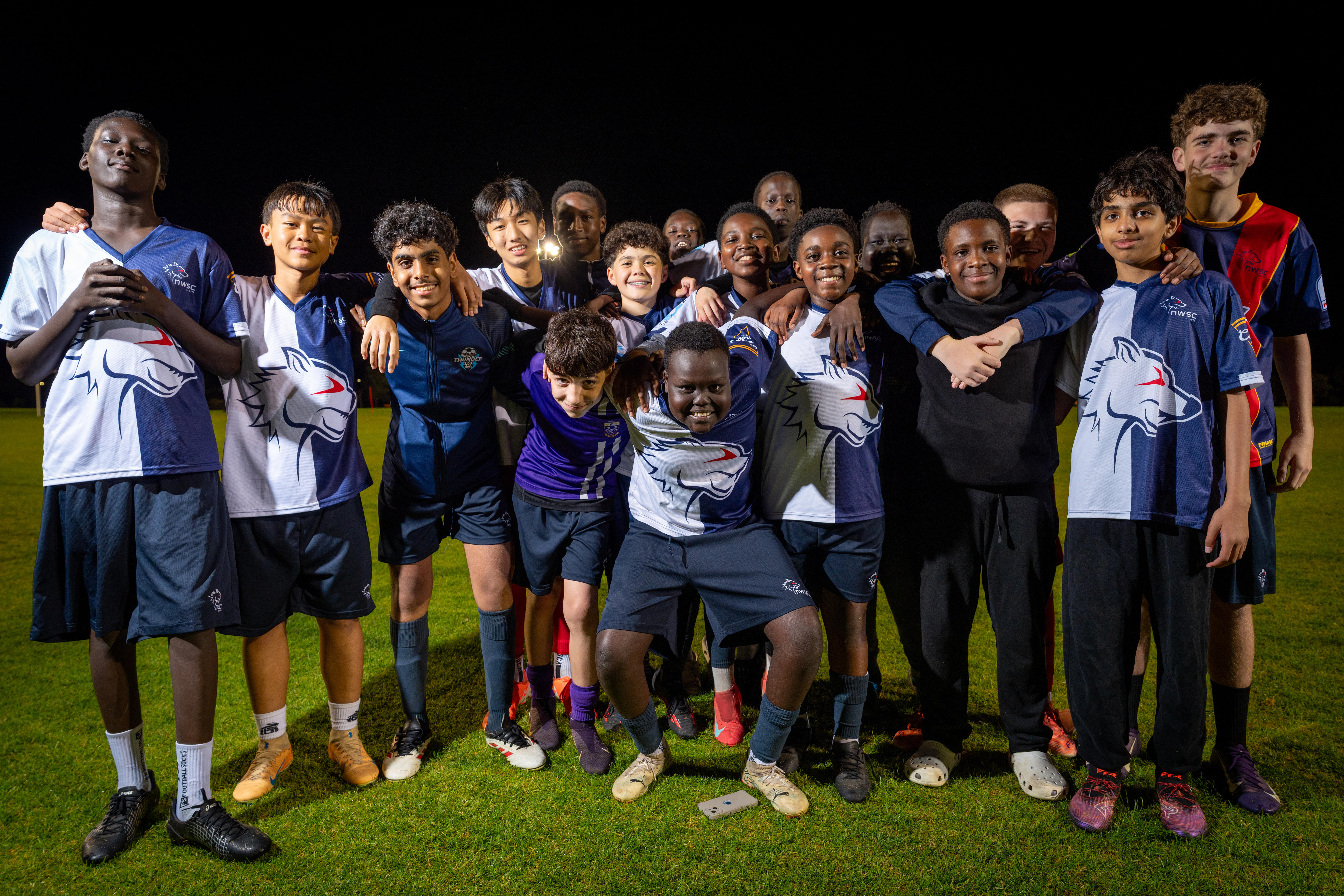 A group of boys in soccer uniforms huddle together, smiling.