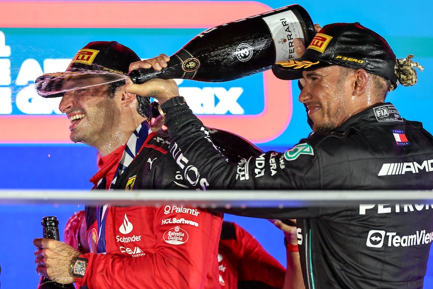 Lewis Hamilton, right, spraying champagne on Ferrari driver Carlos Sainz, on a podium after a night race.