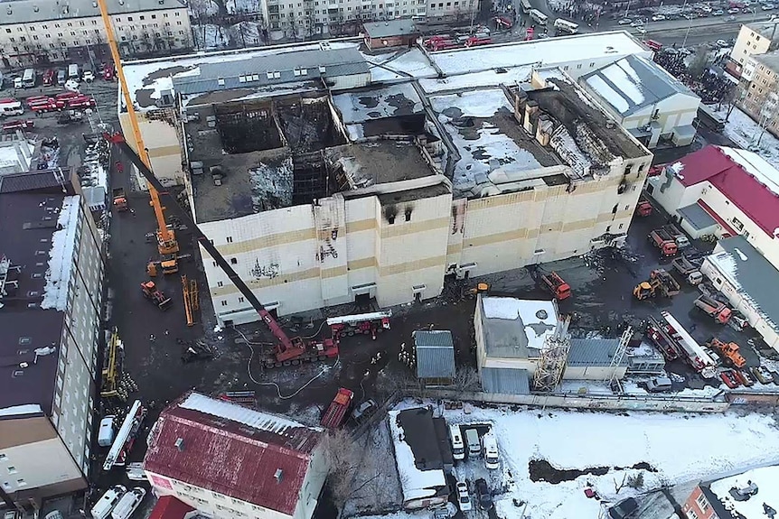 Aerial view of emergency services cleaning up the wreckage around a charred shopping centre.