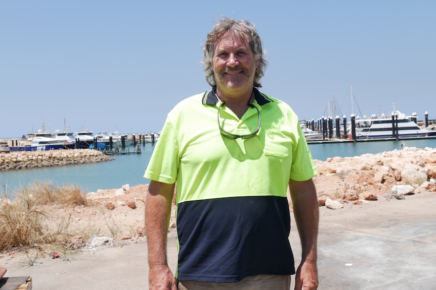 Mark Ferguson - owner of an Exmouth tourism business - stands at a beach wearing a high vis t-shirt. 
